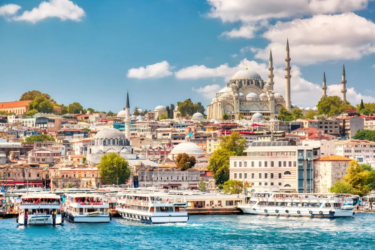 Touristic sightseeing ships in Golden Horn bay of Istanbul and view on Suleymaniye mosque with Sultanahmet district against blue sky and clouds. Istanbul, Turkey during sunny summer day.